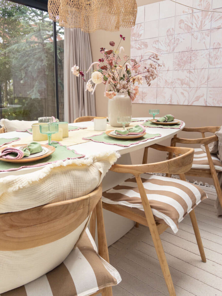Gestylede zomertafel onder een overkapping met linnen tafelloper, bloemen en windlichten in crème en groen